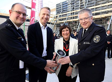 Wichtige Vertreter:innen der BIM und der Berliner Feuerwehr posieren mit einer Zeitkapsel vor einer Baustelle.